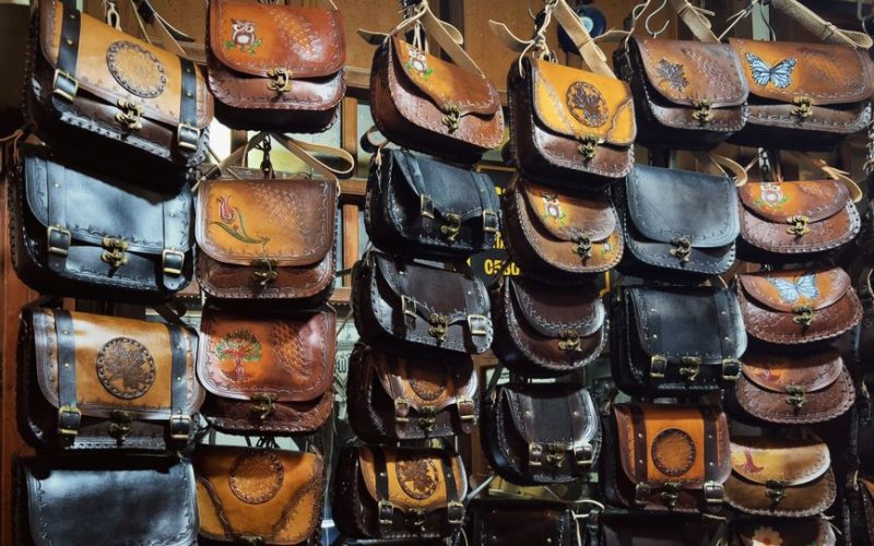 A collection of handcrafted leather bags with artistic designs on display at a shop.