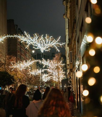 A bustling city street at night adorned with festive Christmas lights on trees and buildings.
